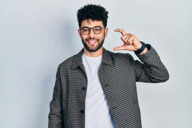 Sakallı, gözlüklü, gülümseyen, kendine güvenen, el hareketleriyle hareket eden, parmaklarıyla işaret yapan ve kameraya bakan genç bir Arap. ölçüm kavramı. 