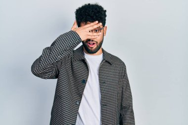 Sakallı genç Arap adam şok içinde yüzünü ve gözlerini kapayarak utangaç ifadesiyle parmaklarının arasından bakıyor.. 