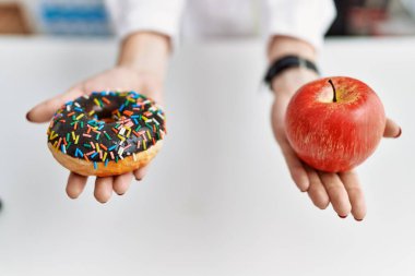 Hastanede elma ve donut taşıyan beslenme uzmanı üniformalı genç bir kadın.
