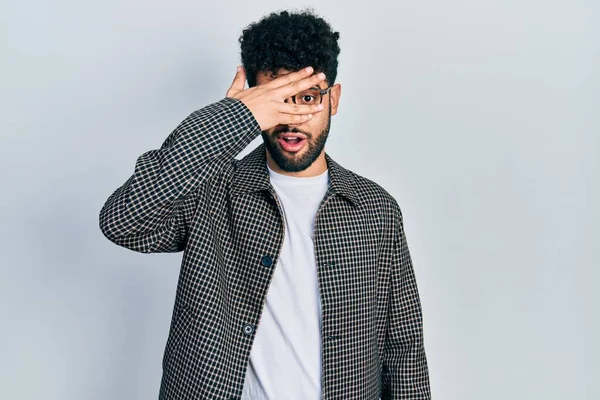 Sakallı genç Arap adam şok içinde yüzünü ve gözlerini kapayarak utangaç ifadesiyle parmaklarının arasından bakıyor.. 