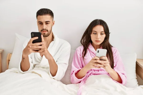 Jovem Casal Hispânico Com Expressão Séria Usando Smartphone Deitado Cama — Fotografia de Stock