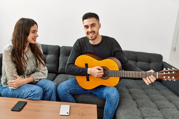 Jovem Casal Hispânico Tocando Guitarra Espanhola Sentado Sofá Casa — Fotografia de Stock