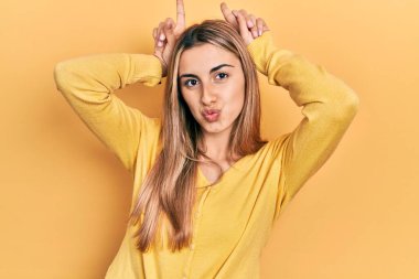 Güzel İspanyol kadın gündelik sarı süveter giyiyor. Komik jestler yapıyor. Parmağını boynuz gibi kafasının üstünde gezdiriyor. 