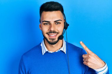 Çağrı merkezinde sakallı operatör kulaklığı takan genç İspanyol adam mutlu bir şekilde elini ve parmağını göstererek gülümsüyor. 