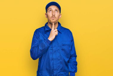 Sakallı, inşaatçı tulumu giyen kel bir adam çenesinde parmak iziyle şüpheyi düşünüp kafasını kaldırıyor. 