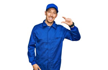 Sakallı, inşaatçı tulumu giyen, gülümseyen, kendine güvenen, el hareketi yapan, parmakları küçük gösteren ve kameraya bakan kel bir adam. ölçüm kavramı. 