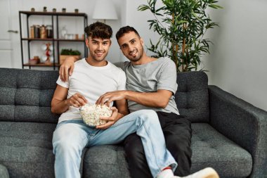 Evdeki kanepede oturup film izleyen iki İspanyol erkek.