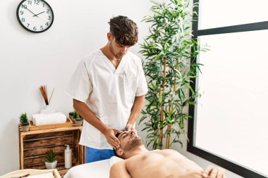 İki İspanyol erkek terapist ve hasta güzellik merkezinde yüz masajı yapıyorlar.