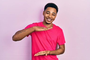 Casua tişörtü giyen genç Afro-Amerikan bir adam. Ellerinde büyük ve büyük bir işaret işareti var. Ölçü sembolü. Kameraya bakıp gülümsüyor. ölçüm kavramı. 