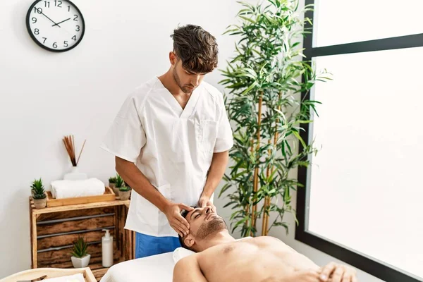 İki İspanyol erkek terapist ve hasta güzellik merkezinde yüz masajı yapıyorlar.