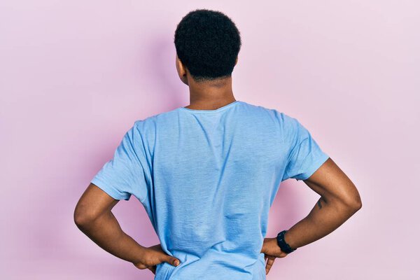Young african american man wearing casual blue t shirt standing backwards looking away with arms on body