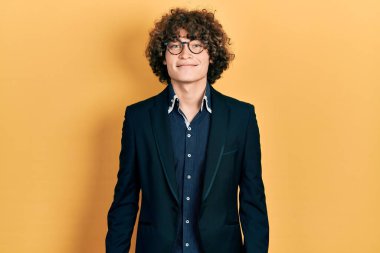 İş ceketi ve gözlük takan yakışıklı genç adam pozitif ve mutlu görünüyor ve kendine güvenen bir gülümsemeyle dişlerini gösteriyor. 