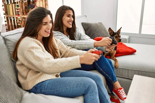 İki kadın evde köpekle oturup video oyunu oynuyor.