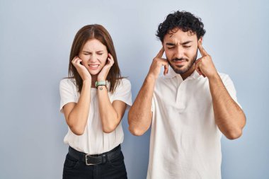 Gündelik kıyafetler giyen genç çift yüksek sesli müzik sesi için kulaklarını parmaklarıyla kapatıyor. sağır kavramı. 