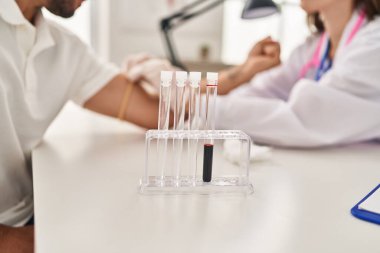 Doktor üniforması giyen kadın ve erkek klinikte kan tahlili yaptırıyor.