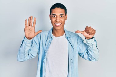 Genç Afro-Amerikalı günlük kıyafetler giymiş altı numarayı gösterip işaret ederken kendinden emin ve mutlu gülümsüyor.. 