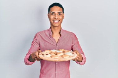 Genç Afro-Amerikan adam elinde pasta tepsisiyle mutlu ve havalı bir gülümsemeyle gülümsüyor. diş gösterme. 