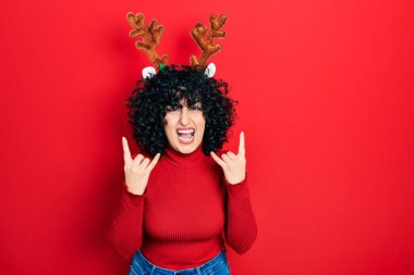 Orta Doğulu genç bir kadın şirin Noel geyiği boynuzları takıyor çılgın bir ifadeyle bağırıyor elleri havada rock sembolü yapıyor. Müzik yıldızı. ağır kavram. 