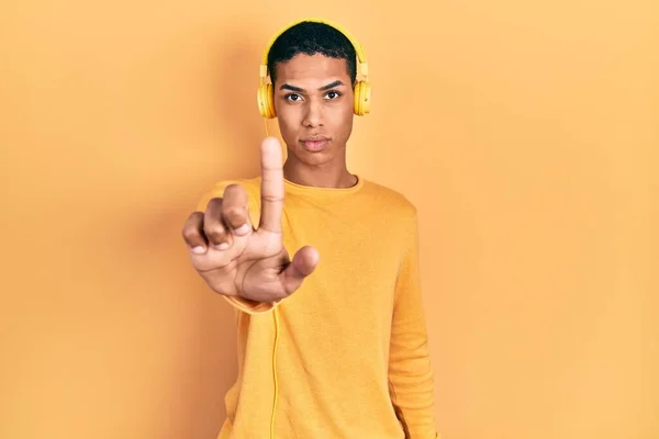 一个年轻的非洲裔美国人 一边用耳机听着音乐 一边用手指尖着 满脸怒容 毫无表情 — 图库照片