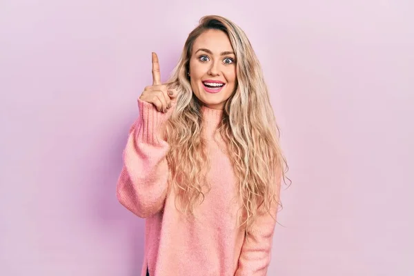 ピンクのセーターを着て美しい若いブロンドの女性は 成功したアイデアで指を指しています 興奮して幸せよ 第1位 — ストック写真