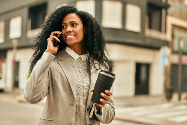 Orta yaşlı Afro-Amerikan iş kadını akıllı telefondan konuşuyor ve şehirde kahve içiyor..