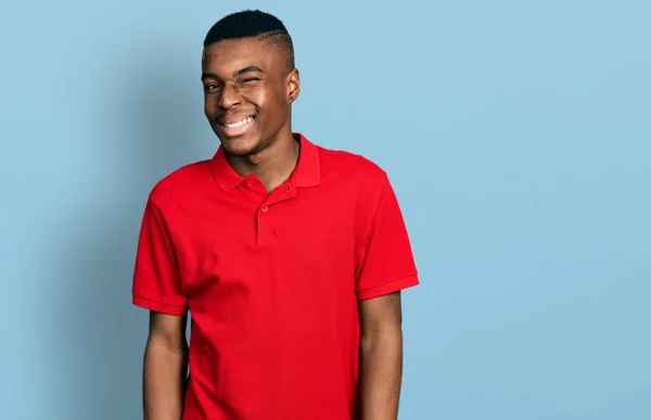 身穿休闲红T恤的年轻的非洲裔美国男人眨着眼睛 带着性感的表情 开朗而快乐地看着摄像机 — 图库照片