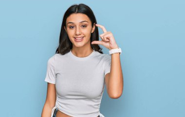 Günlük beyaz tişört giyen, gülümseyen, kendine güvenen, el hareketi yapan, parmaklarıyla işaret yapan ve kameraya bakan genç İspanyol kız. ölçüm kavramı. 