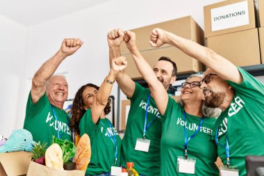 Bir grup orta yaşlı gönüllü, yardım merkezinde yumrukları havada mutlu gülümsüyor..