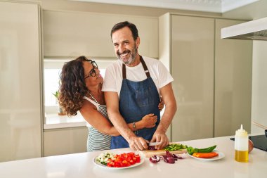 Orta yaşlı İspanyol çift gülümsüyor. Kendilerine güveniyorlar ve mutfakta yemek pişiriyorlar.