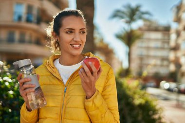 Genç İspanyol kız şehirde bir şişe su içip elma yiyor..