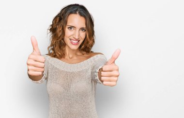 Güzel, beyaz bir kadın günlük giysiler giyip, olumlu bir jest yapıyor, gülümsüyor ve başarı için seviniyor. kazanan jest. 