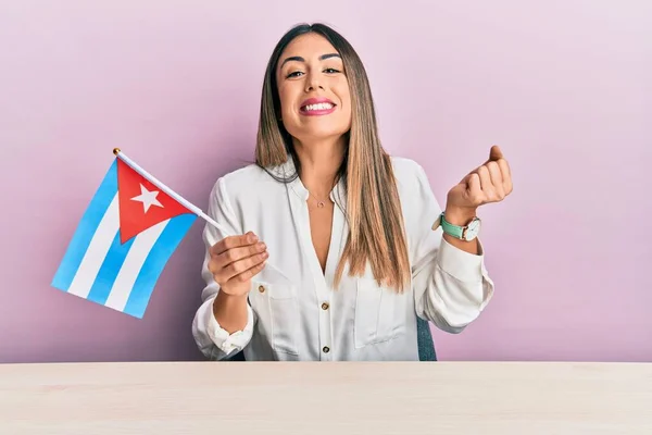 テーブルの上に座ってキューバ国旗を持っている若いヒスパニック系の女性は誇りを叫びます 勝利と成功を祝う非常に腕を上げ興奮して — ストック写真