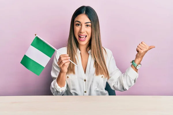 Ung Latinamerikansk Kvinna Håller Nigeria Flagga Sitter Bordet Pekar Tummen — Stockfoto