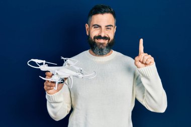 İHA 'yı elinde tutan genç İspanyol bir adam bir fikir veya soruyla gülümsüyor ve mutlu bir yüzle işaret ediyor. 