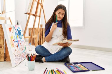 Sanat stüdyosundaki not defterine şüphe ifadesi çizen genç Latin kadın.