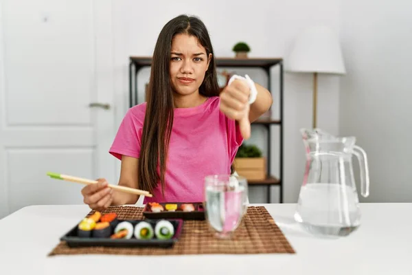 箸を使って寿司を食べる若いブルネットの女性は 親指を下にジェスチャーで拒絶と否定を示す不満と怒りを見ている 悪い表現 — ストック写真