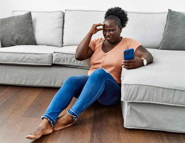 非洲年轻的非洲女人坐在家里用智能手机的年轻的非洲女人忧心忡忡 — 图库照片