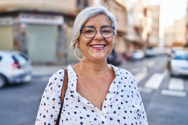 Orta yaşlı bir kadın sokakta kendine güvenerek gülümsüyor.