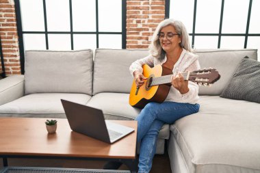 Orta yaşlı bir kadının evde online gitar dersi var.