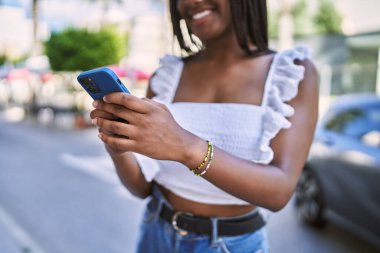 Genç Afrikalı Amerikalı kız şehirde akıllı telefon kullanarak mutlu bir şekilde gülümsüyor..