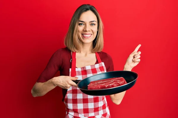 Νεαρή Καυκάσια Ξανθιά Γυναίκα Φορώντας Μαγειρεμένη Ποδιά Μαγειρεύοντας Κρέας Στο — Φωτογραφία Αρχείου