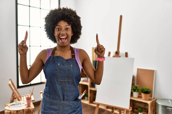若いですアフリカ系アメリカ人女性とともにアフロヘアでアートスタジオで笑顔と驚きと指と腕を上げて — ストック写真