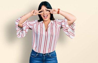 Gündelik kıyafetler giyen genç İspanyol kız barış sembolü yapıyor. Yüzünde parmaklar, gülümseyerek zaferi gösteriyor. 