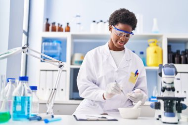 Laboratuvarda çalışan, bilim adamı üniforması giyen Afrikalı Amerikalı kadın.