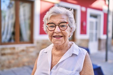 Yaşlı, kır saçlı, gülümseyen bir kadın sokakta kendine güveniyor.