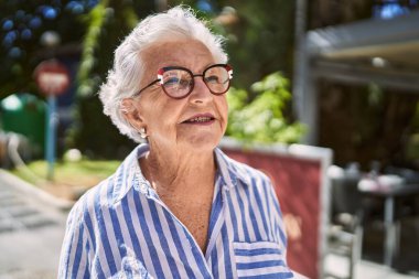 Yaşlı, kır saçlı, gülümseyen bir kadın sokakta kendine güveniyor.