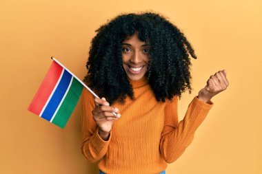 Afro saçlı, gambiya bayrağı tutan Afrikalı Amerikalı bir kadın gururla bağırıyor, zaferi ve başarıyı kutluyor. 