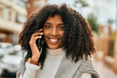 Genç Afrikalı Amerikalı kadın gülümsüyor. Şehirdeki akıllı telefondan mutlu bir şekilde konuşuyor..