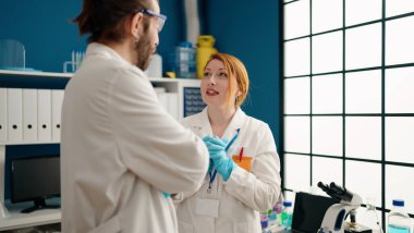 Laboratuvarda konuşan bilim adamı üniforması giyen kadın ve erkek.