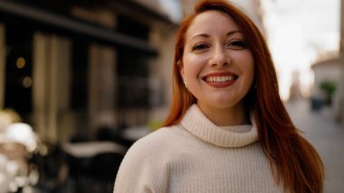 Genç, kızıl saçlı, kendine güvenen bir kadın sokakta yürüyor.